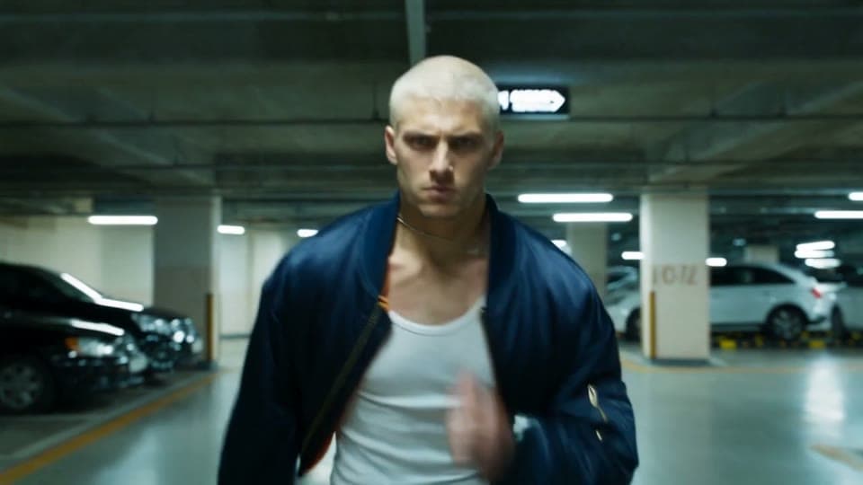 Reference clip: a man in a bomber jacket runs at the camera through a parking garage